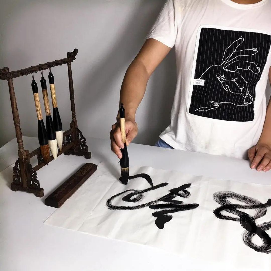 Conjunto completo de pincéis chineses tradicionais, ideal para caligrafia e pintura de festivais. Detalhe dos pincéis de cabelo de lobo e ovelha, mostrando a qualidade das cerdas. Artista usando pincéis em caligrafia chinesa, realçando a precisão e flexibilidade. Embalagem elegante do conjunto de pincéis, destacando a tradição e a qualidade.