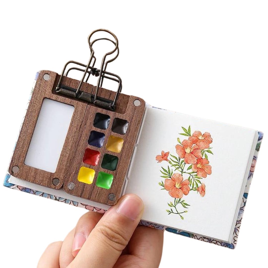 Caixa de pintura portátil Outdoor Sketch fechada em madeira de nogueira preta, exibindo o acabamento elegante. Interior da caixa de pintura portátil Outdoor Sketch, mostrando os 8 compartimentos vazios. Mini caixa de pintura Outdoor Sketch sendo usada ao ar livre, destacando sua portabilidade e funcionalidade. Close-up no clipe de bronze da caixa de pintura Outdoor Sketch, um acessório prático para artistas.