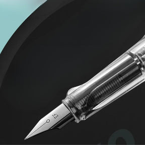 Caneta-tinteiro transparente com design moderno ao lado de cartuchos de tinta.
Escrita elegante e suave demonstrada em papel com a caneta em uso.